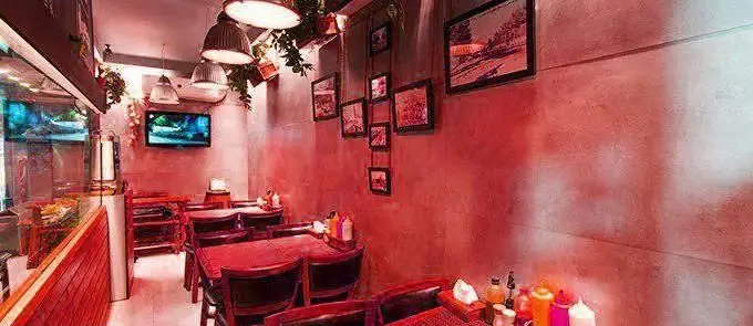 فضای داخلی دنج و شیک برگر بار با نورپردازی قرمز گرم، دکوراسیون مدرن، میز و صندلی‌های چوبی و تلویزیون، آماده میزبانی از مشتریان.