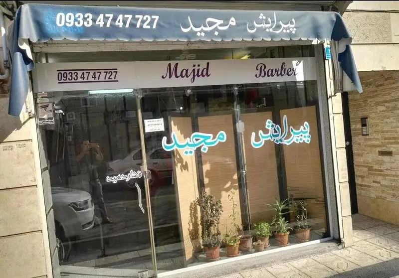 نمای بیرونی پیرایشگاه مردانه مجید با تابلو و شیشه سکوریت به همراه شماره تماس جهت رزرو نوبت اصلاح مو و صورت آقایان