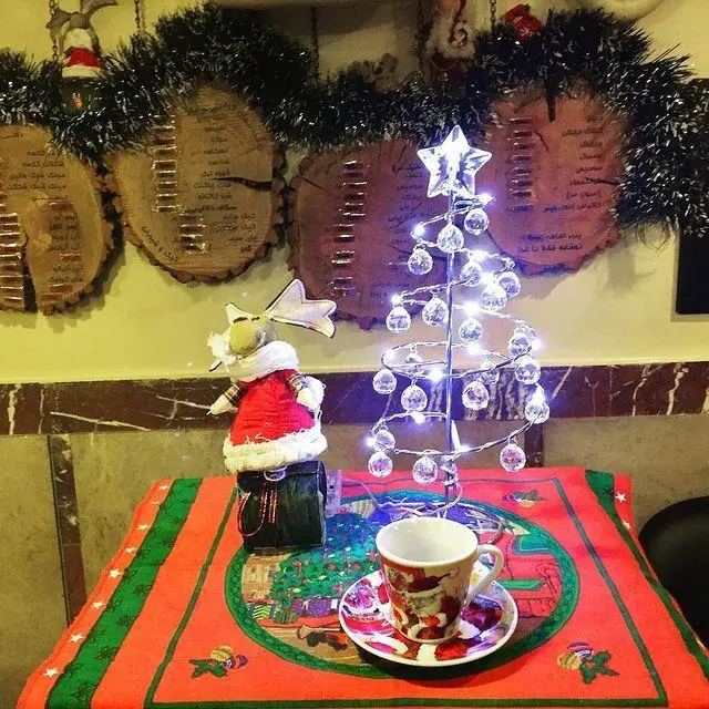 دکوراسیون زیبای کریسمس در کافه لینت: درخت نورانی، فنجان قهوه و عروسک گوزن بامزه. فضایی دلنشین برای لذت بردن از نوشیدنی‌های گرم در تعطیلات.