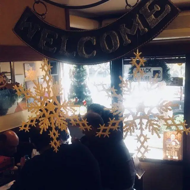 دکوراسیون کریسمسی و دنج کافه لینت با تابلو 'WELCOME' و برف‌های طلایی، فضایی دلنشین برای مشتریان فراهم کرده است.