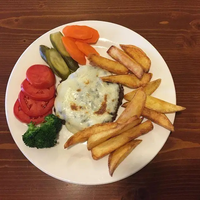 وعده غذایی اشتهاآور در کافه لینت: یک همبرگر پنیری آبدار با سیب‌زمینی وجز طلایی، گوجه، خیارشور و سبزیجات تازه و سالم.