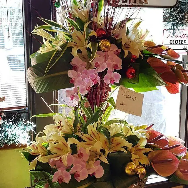 گل‌آرایی باشکوه و چشم‌نواز نوروزی در کافه لینت شامل لیلیوم‌های زرد، ارکیده‌های صورتی و گل‌های آنتوریوم قرمز با تزئینات شاد.