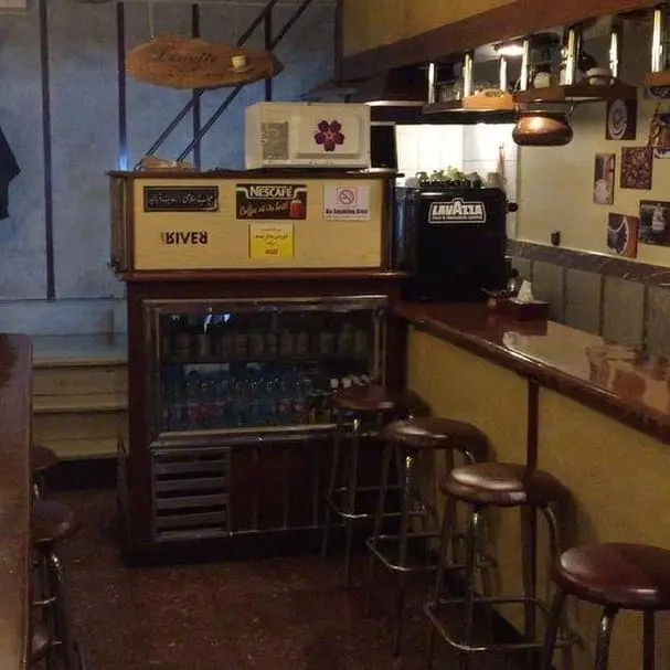 نمایی داخلی و گرم از کافه لینت با میز بار چوبی، صندلی‌های شیک، یخچال نوشیدنی و دستگاه‌های قهوه لاواتزا و نسکافه. فضایی دلنشین برای مشتریان.