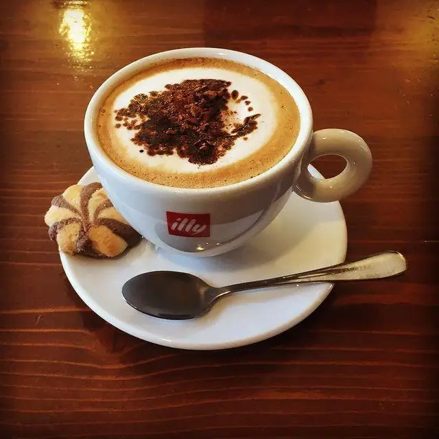 قهوه کاپوچینو Illy گرم و خوشمزه با پودر کاکائو و کوکی راه راه در محیط دلنشین کافه لینت. مناسب برای صبحانه و عصرانه.