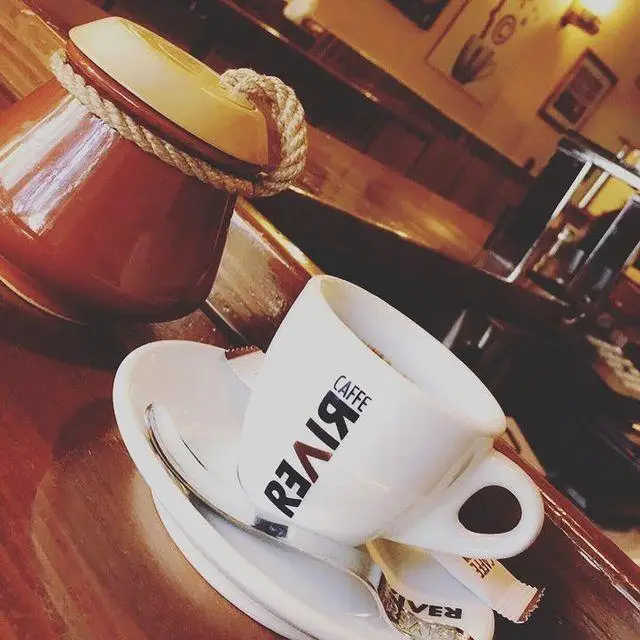 یک فنجان قهوه اسپرسو کافه ریور روی میز چوبی در محیط گرم و دلنشین کافه لینت. این تصویر حس آرامش و لذت نوشیدن قهوه را به خوبی منتقل می‌کند.