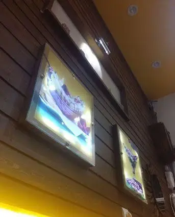 فضای داخلی جذاب و مدرن رستوران موسوی: دیوارهای چوبی، تابلوهای نورانی هنری از دسر و بستنی‌های خوش‌رنگ، سقف نارنجی روشن با نورپردازی.