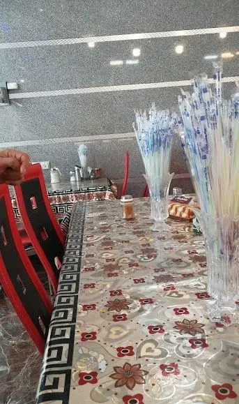 رستوران موسوی: فضای داخلی دلنشین با میزهای طرح‌دار، صندلی‌های قرمز و گلدان‌های پر از نی نوشیدنی. آماده پذیرایی از شما.