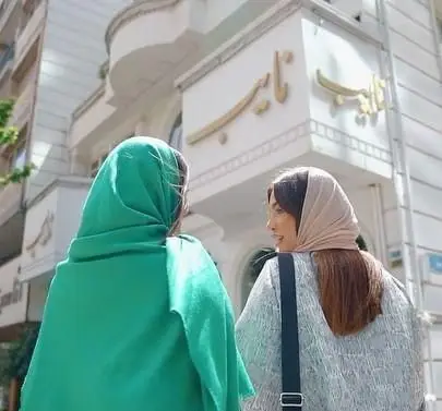 دو بانوی محجبه در حال قدم زدن در حوالی بوفه نایب ساعی. تابلوی طلایی نایب جلوه‌ای ویژه به این رستوران در تهران بخشیده است.