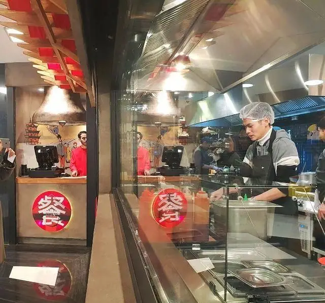 نمایی داخلی از رستوران آسیایی بامبو اکسپرس، آشپزخانه اپن با سرآشپز در حال پخت غذا و پیشخوان سفارشات با لوگوی 餐.