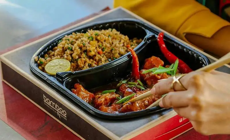 غذای خوشمزه آسیایی از رستوران بامبو اکسپرس شامل برنج سرخ شده با سبزیجات و مرغ با سس تند در بسته بندی آماده و شیک