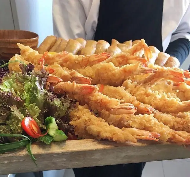 سینی بزرگ و اشتهاآور میگو تمپورا طلایی و ترد در رستوران بامبو اکسپرس، همراه با سالاد تازه. بهترین غذای آسیایی را تجربه کنید.