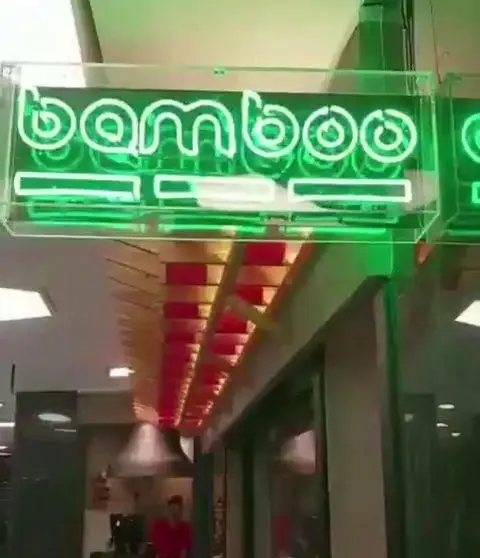 رستوران بامبو اکسپرس: تابلو نئونی سبز "bamboo" در ورودی، با دکوراسیون چوبی و فضای داخلی پرنور و مدرن.