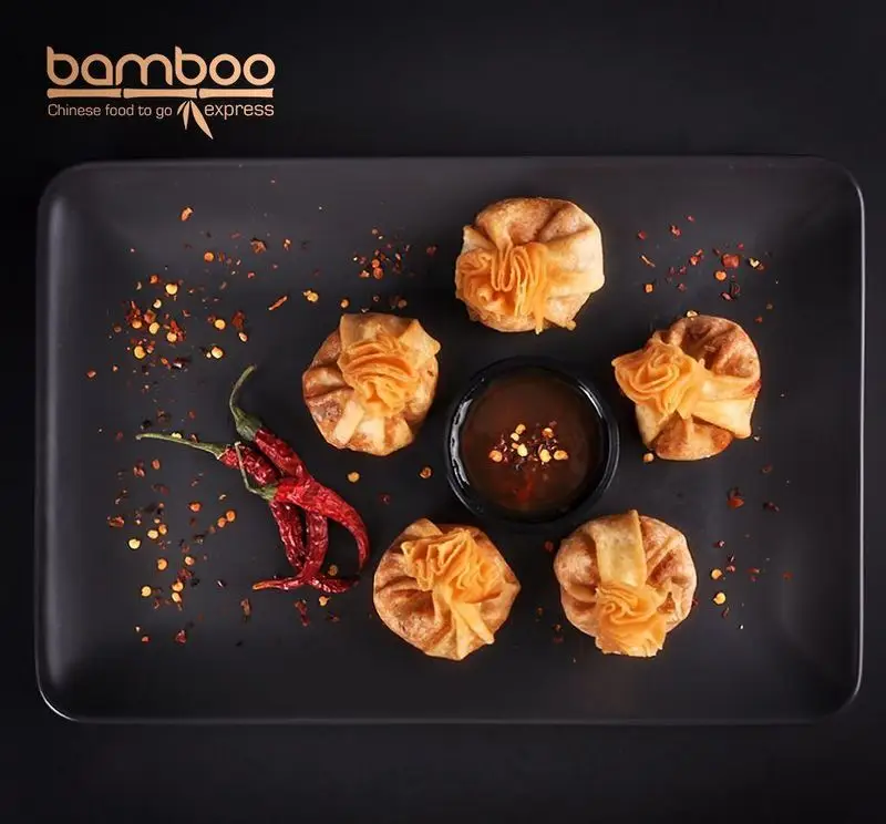 وانتون سرخ شده Bamboo Express: غذای چینی آماده، شش وانتون طلایی و ترد با سس تند، فلفل قرمز و پرک چیلی روی بشقاب مشکی.