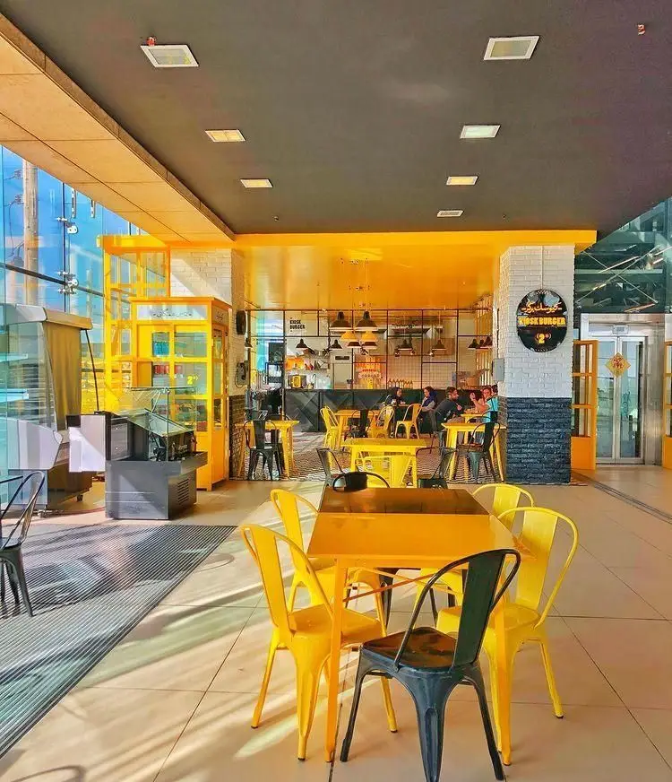 تصویری از محیط داخلی و دکوراسیون جذاب فست فود کیوسک برگر با مبلمان زرد و مشکی، فضایی مدرن و روشن برای مشتریان.