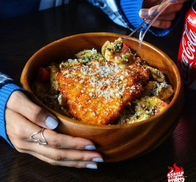 پاستا و فیله مرغ سوخاری ترد با پنیر فراوان در کاسه چوبی، غذای محبوب فست فود آگرین. تجربه‌ای خوشمزه و کامل.