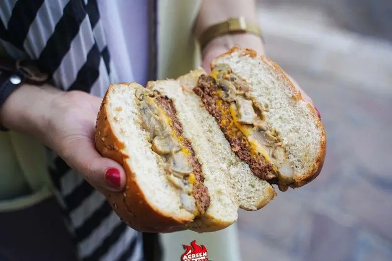 همبرگر قارچ و پنیر لذیذ فست فود آگرین، نصف شده در دستان یک نفر، با نمایش واضح لایه‌های برگر گوشت، پنیر آب شده و سس قارچ.