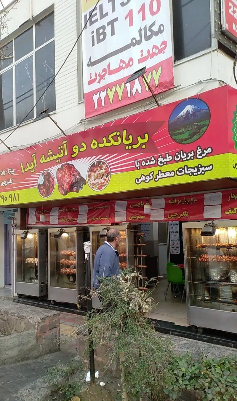 نمای فست فود و بریانکده دوآتیشه آیدا، با بنر تبلیغ مرغ بریان طبخ شده با سبزیجات معطر کوهی، پیتزا و غذاهای خوشمزه.