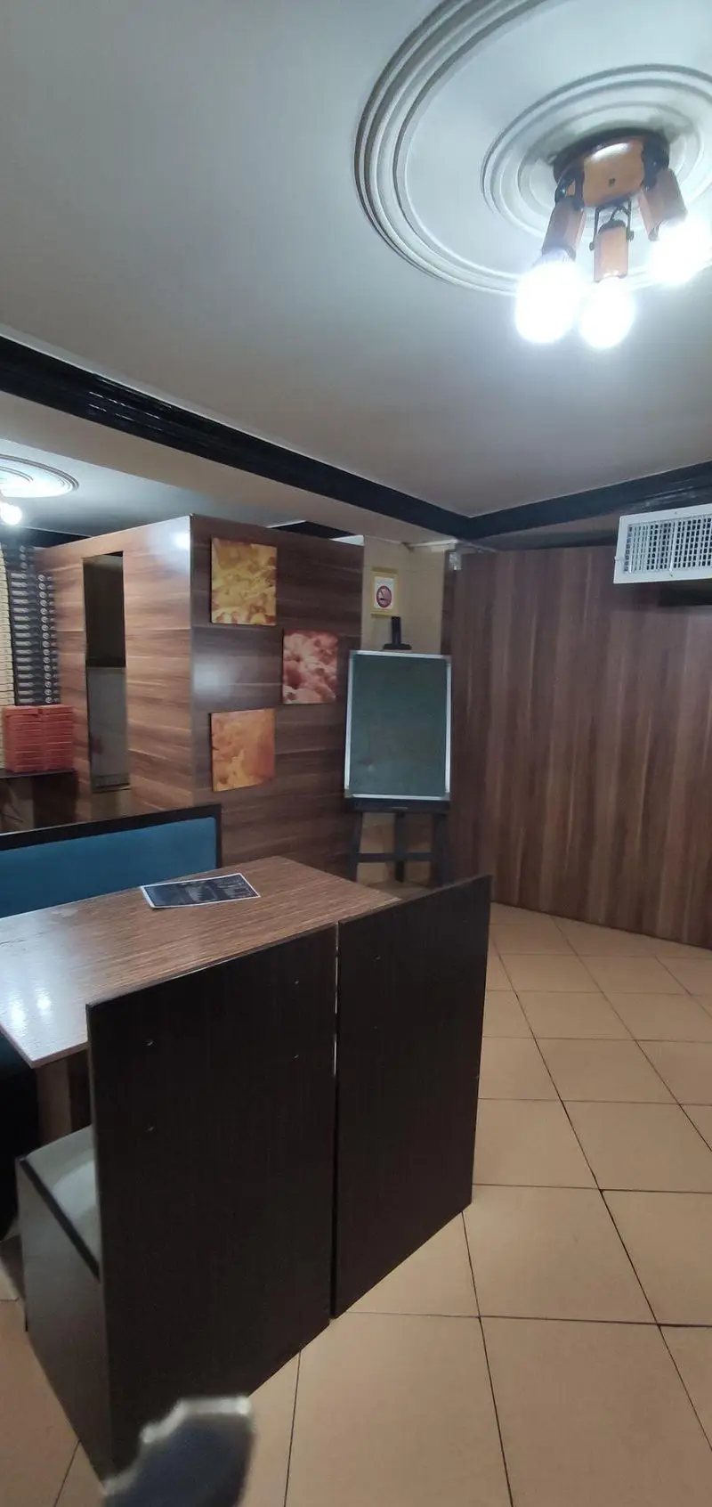 نمایی از فضای داخلی فست فود جزیره: میز و صندلی چوبی، دیوارپوش‌های مدرن، نورپردازی سقف و تابلوهای تزئینی برای محیطی دنج و گرم.