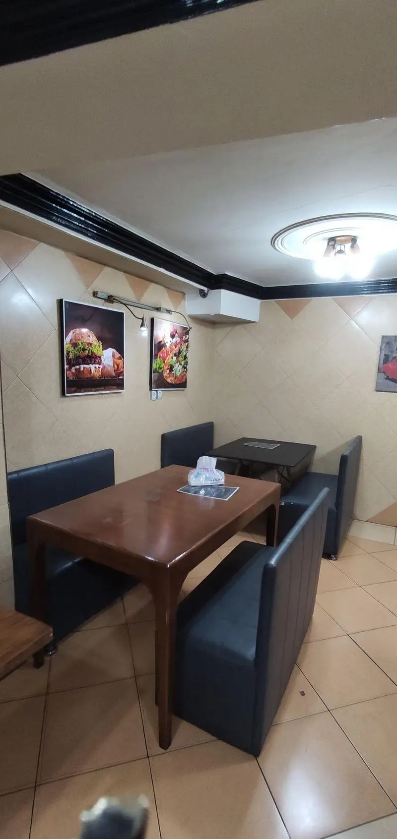 تصویری از فضای داخلی فست فود جزیره، دارای دکوراسیونی مدرن با دیوارهای طرح‌دار و تابلوهای همبرگر و پیتزا، میزهای چوبی و مبلمان راحت.