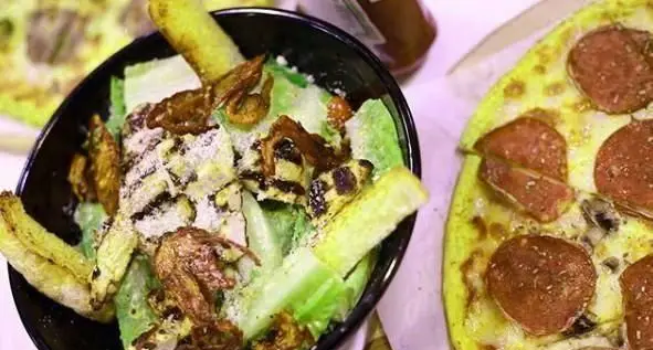 پیتزا پپرونی و قارچ با خمیر زرد، در کنار سالاد سزار تازه با کاهوی سبز، تکه‌های مرغ گریل و پنیر پارمزان در کافی شاپ سیمو.