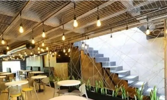 دکوراسیون داخلی کافی شاپ سیمو با سبک صنعتی-مدرن، نورپردازی خاص لامپ‌های ادیسونی، سقف مشبک و پله‌های هندسی جذاب.