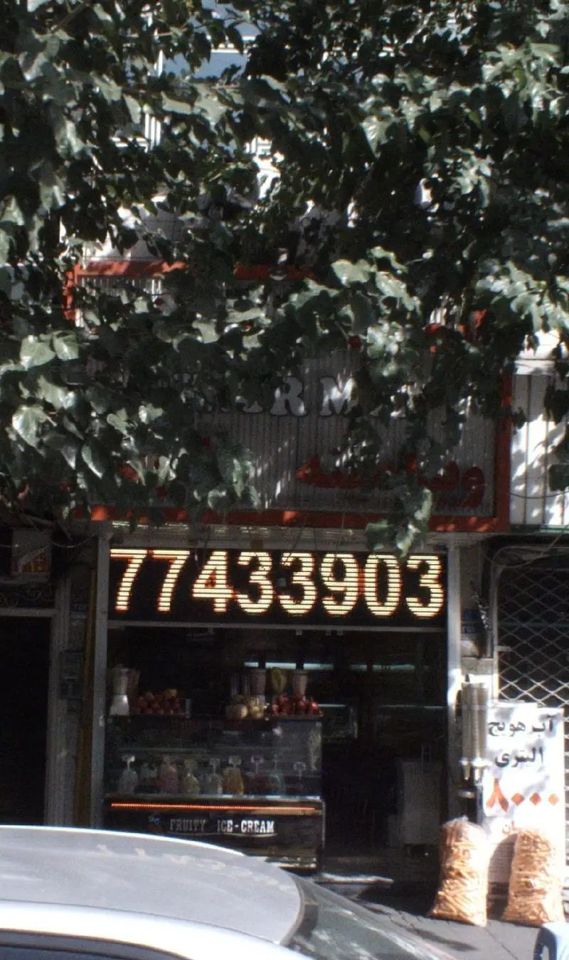 نمایی از مغازه ویتامینه و آبمیوه فروشی با تابلوی LED شماره تلفن 77433903، عرضه کننده آبمیوه طبیعی، بستنی میوه‌ای و شیک‌های تازه.