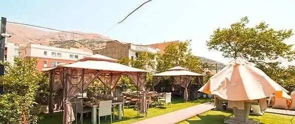 فضای باز دلنشین کافی شاپ شاندیز اعیانی با آلاچیق‌های دنج و شیک، میز و صندلی‌های راحت، چمنزار سرسبز و چشم‌انداز کوهستانی.