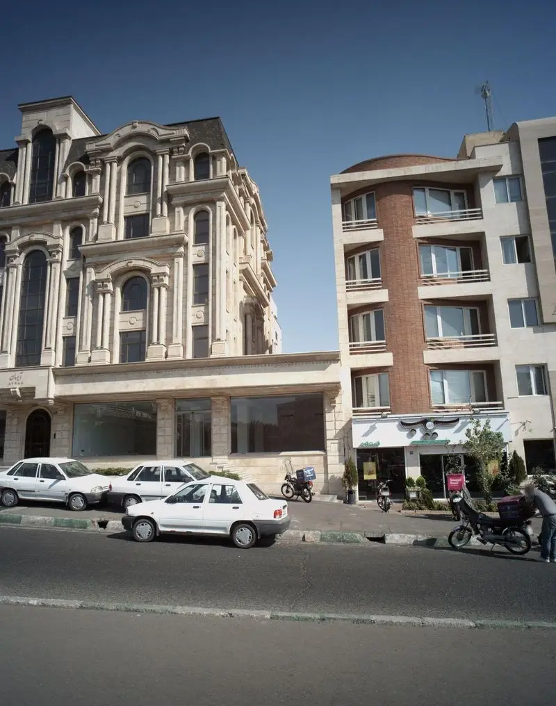 نمای بیرونی فست فود سیب ۳۶۰ در خیابان، با معماری شهری متنوع، خودروهای پارک شده و موتورهای دلیوری.