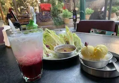میز چیده شده در کافه روحی باغ نگارستان: نوشیدنی خنک لایه ای، سالاد کاهو با سس و سه اسکوپ بستنی زرد. تجربه ای دلپذیر در فضای سبز.