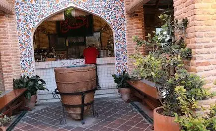 تصویری از کافه روحی در محوطه باغ نگارستان، شامل فضای باز با آجرکاری و کاشی‌کاری سنتی، گلدان سفالی بزرگ و گیاهان سبز.