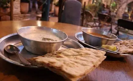 میز غذای کافه روحی در محوطه باغ نگارستان شامل نان تازه، دو نوع خوراک یا سوپ در کاسه‌های فلزی با دیزاینی سنتی و دلنشین.