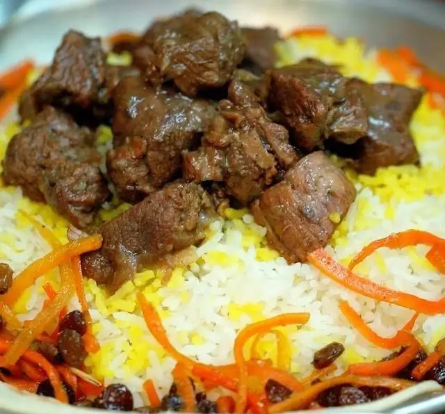 یک بشقاب پلو گوشت زعفرانی خوشمزه و سنتی به همراه هویج و کشمش، سرو شده در کافه روحی باغ نگارستان، تجربه ای اصیل از غذای ایرانی.