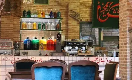 فضای دلنشین کافه روحی در باغ نگارستان با دکوراسیون آجری، قفسه نوشیدنی‌های رنگی، میز بار مجهز به دستگاه قهوه‌ساز و صندلی‌های راحت آبی.