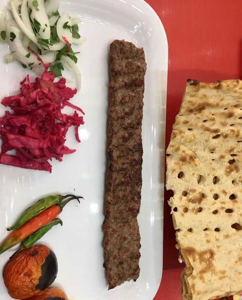 کباب بناب لذیذ رستوران سنتی افق بناب، با مخلفات تازه شامل پیاز، ترشی کلم، فلفل کبابی و نان داغ برای غذای اصیل ایرانی.