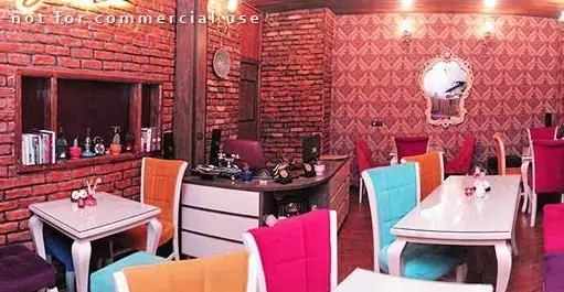 تصویر فضای داخلی رستوران کلاسیک و شیک با دیوارهای آجری و طرح‌دار قرمز، میزهای سفید و صندلی‌های رنگارنگ و دلنشین.