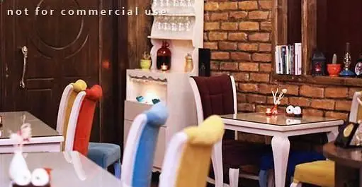 نمایی از فضای داخلی رستوران کلاسیک با دکوراسیون دنج و شیک، شامل میز و صندلی های مدرن و رنگی، دیوار آجری و المان های چوبی با نورپردازی گرم.