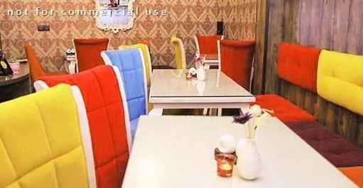 فضای داخلی دنج رستوران کلاسیک با میزهای براق سفید و صندلی‌های شاداب رنگارنگ زرد، قرمز، آبی، همراه با نیمکت‌های مدرن.