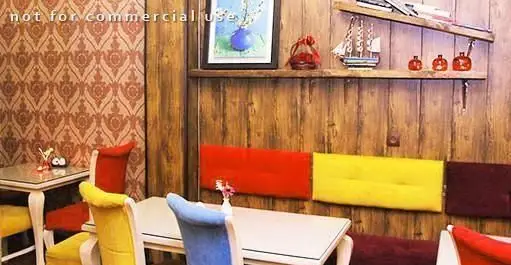 دکوراسیون داخلی رستوران کلاسیک، با دیوارپوش طرح‌دار، پنل‌های چوبی، میزهای روشن و صندلی‌های رنگارنگ قرمز، زرد و آبی.