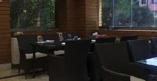 فضای داخلی دلنشین رستوران ایرانی نوید با میز و صندلی‌های شیک حصیری و چشم‌انداز زیبای فضای سبز بیرون، آماده پذیرایی از میهمانان.