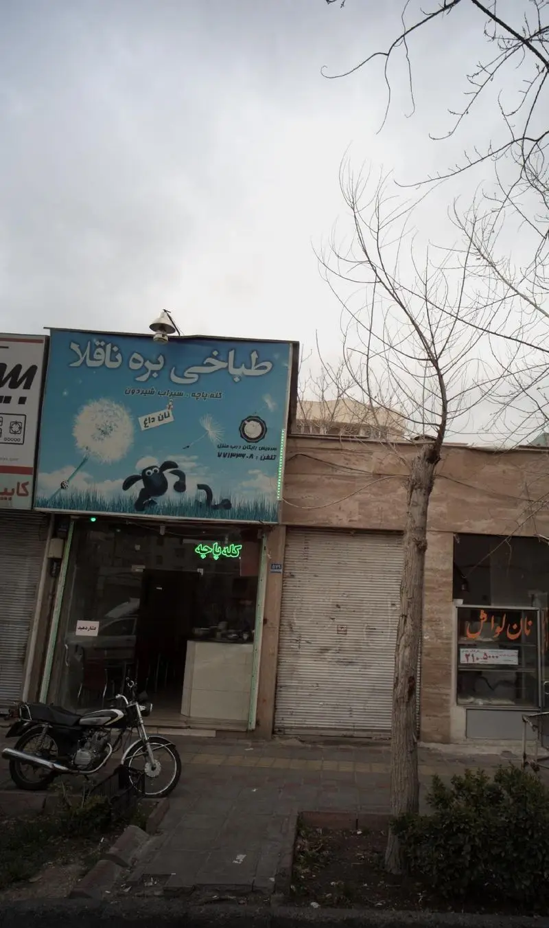 طباخی بره ناقلا، رستوران کله پاچه و سیرابی شیردون با نان داغ در نمای خیابان، همراه با موتور سیکلت پارک شده.