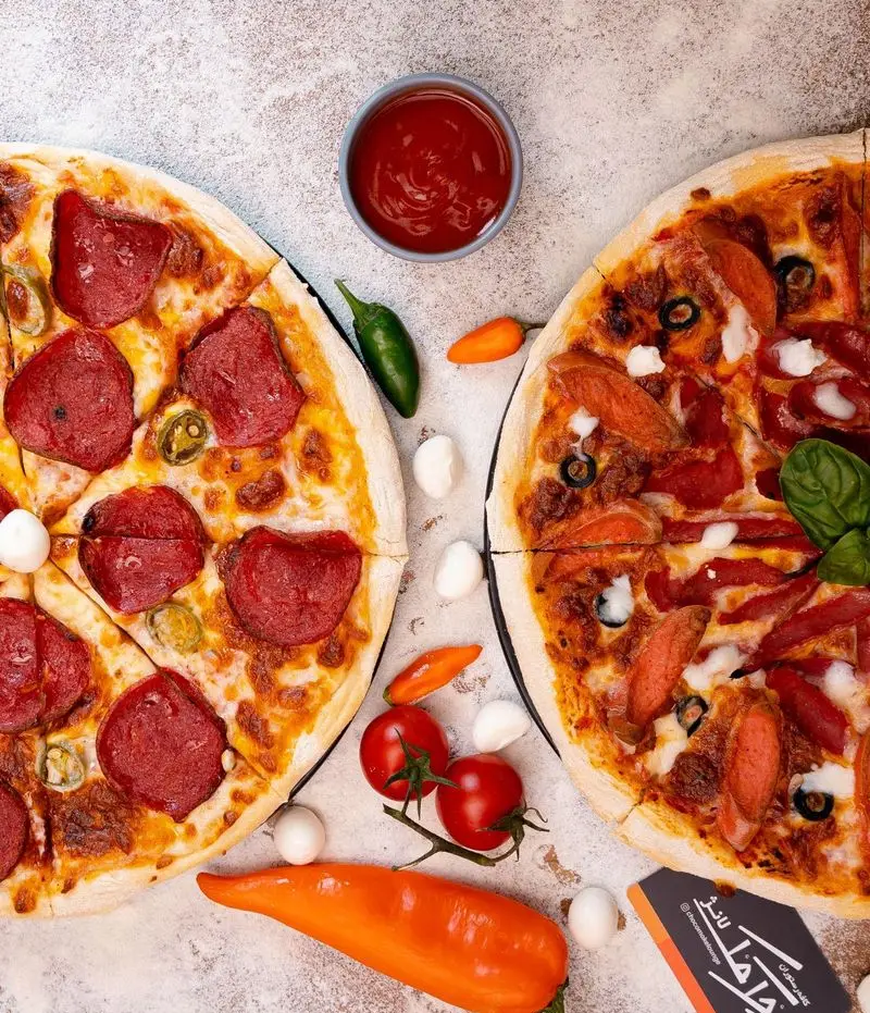 تصویر دو پیتزا پپرونی و سوسیس لذیذ کافه رستوران چک مک لانژ با مواد اولیه تازه شامل فلفل، گوجه و پنیر موزارلا.