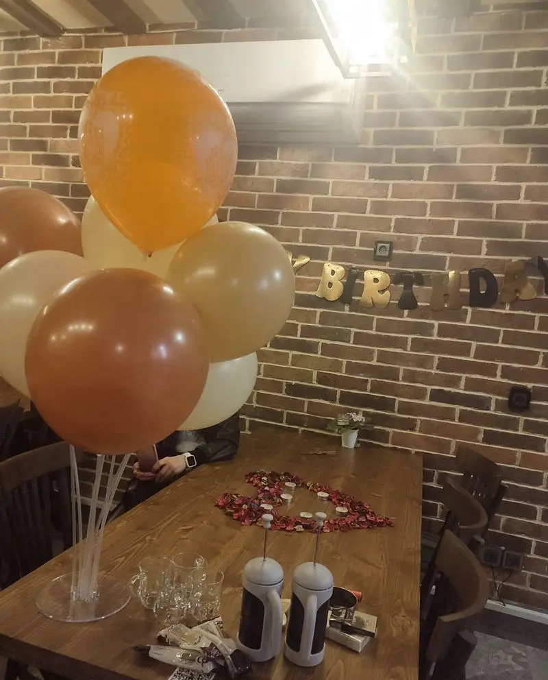 دکوراسیون جشن تولد در کافه رستوران چک مک لانژ، شامل بالون‌های رنگی، بنر تولد و میز چوبی با شمع و گلبرگ‌های قلبی شکل.