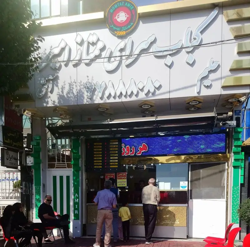 تصویر نمای بیرونی و شلوغ کباب سرای ممتاز امیر، یک رستوران محبوب کباب در ایران، با تابلوی روشن و مشتریان حاضر.