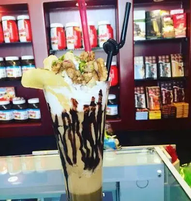 میلکشیک ویژه نوتلا با تزئین خامه فراوان، آجیل تازه و موز، نمایشی دلربا از دسرهای لذیذ کافی شاپ گل یخ.