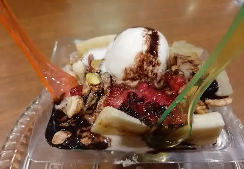 دسر مخصوص کافی شاپ گل یخ شامل بستنی، میوه های تازه و سس شکلات، تزیین شده با آجیل و پسته برای تجربه ای شیرین و دلنشین.