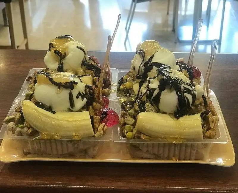 دو پرس دسر ویژه بستنی و موز کافه گل یخ با تزئین سیروپ شکلات، عسل، پسته و گردو، تجربه طعمی بی‌نظیر.