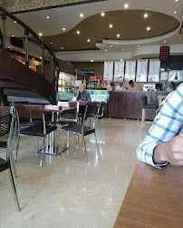 تصویری از فضای داخلی مدرن و دلنشین کافی شاپ گل یخ با میز و صندلی‌های راحت، مشتریان و نورپردازی گرم، محیطی آرام برای کافه.