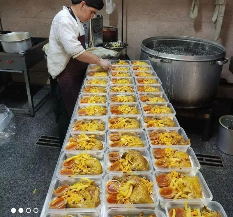 آشپز رستوران آویشن در حال بسته‌بندی بهداشتی و انبوه وعده‌های غذایی شامل مرغ، برنج، مخلفات و سس در ظروف بیرون‌بر.