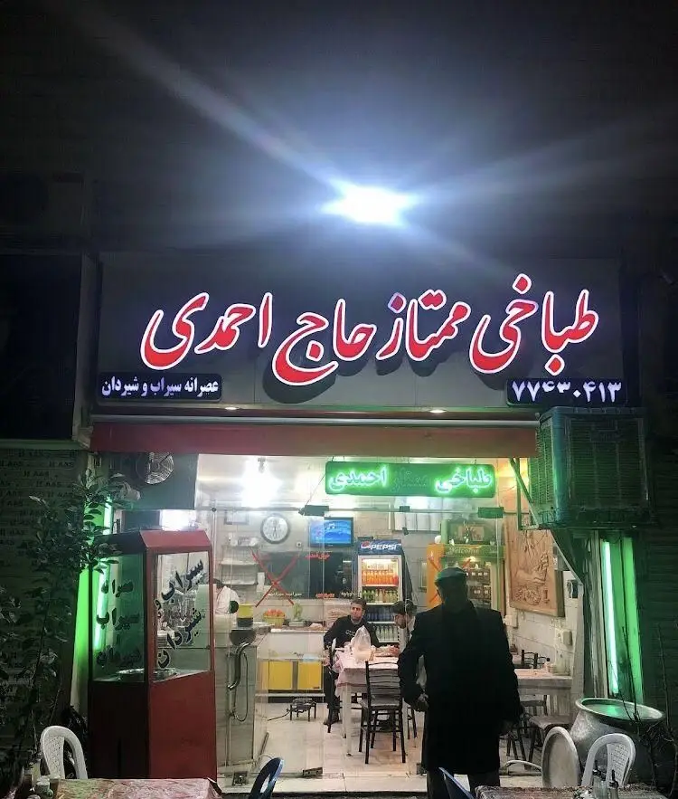 طباخی ممتاز حاج احمدی: نمای شبانه با تابلوی نئون روشن، شماره تماس ٧٧٣٠.۴١٣ و عصرانه سیراب و شیردان. آماده پذیرایی از مشتریان.