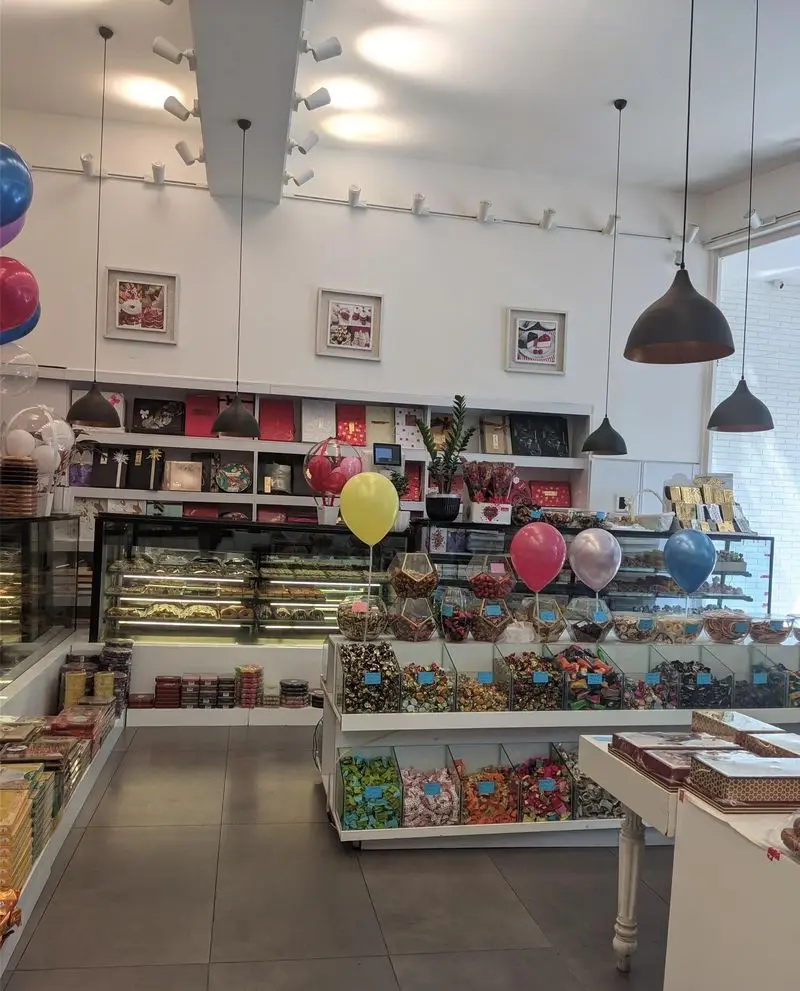 نمای داخلی فروشگاه نان و شیرینی لادن غرب با ویترین‌های پر از شیرینی، شکلات و آبنبات‌های رنگارنگ در محیطی شیک و روشن.